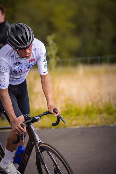 The man is riding a bike in a field. He has the word wielrennen on his jersey and is wearing a black helmet.