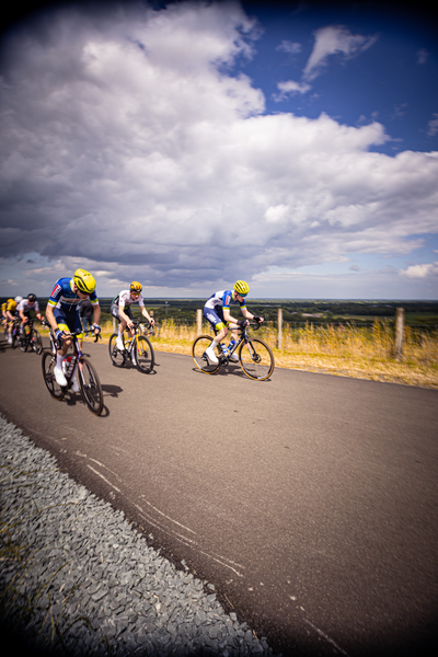 A group of men are riding bicycles on the road. They all have yellow helmets.