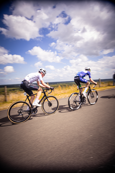 Two cyclists are in a race on the road, wearing helmets and blue and white shirts.