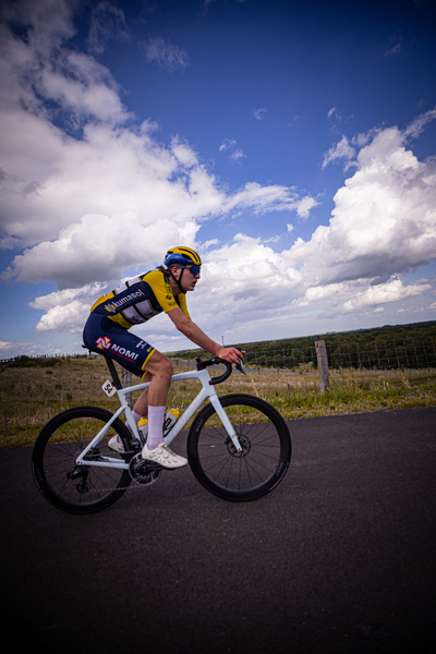 A young man on a white bike with blue and yellow jersey rides down a road.