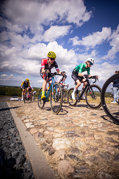 A group of cyclists race through a cobblestone street during the Nederlands Kampioenschap.