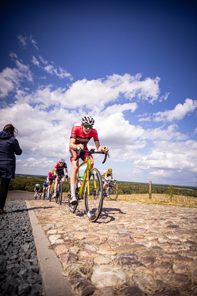 A group of young cyclists race on a cobblestone street.