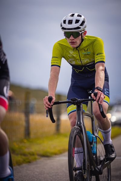 A boy is riding a bicycle with a yellow shirt on that says "Nederlandse banner".