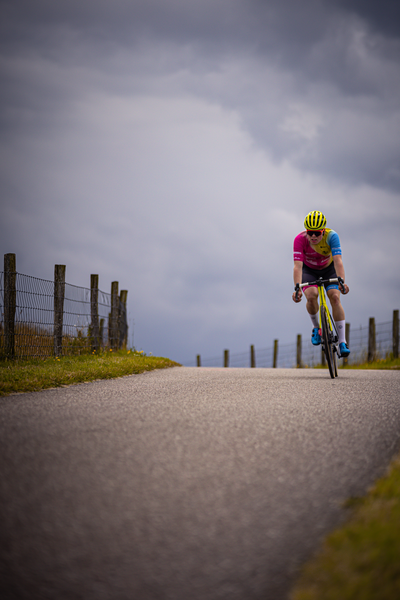 A man in a pink and blue outfit rides a bicycle down the road.