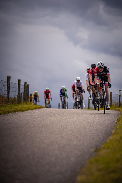 A group of cyclists riding on a road with one in the lead and another following behind.