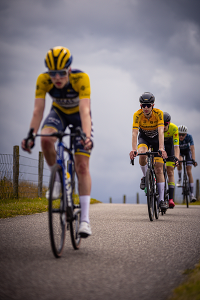 The Juniors, wearing colorful jerseys and black helmets, ride their bikes on a country road.