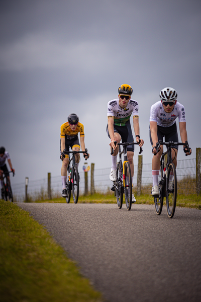 Three cyclists are riding down a rural road during the Nederlands Kampioenschap.