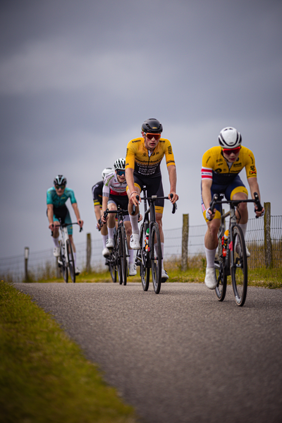 Six cyclists are riding on a road in the Netherlands during a race.