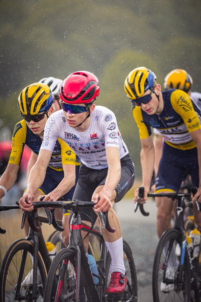 A bicycle race is taking place and a young man is riding his bike wearing a red helmet.