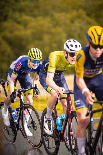 A group of young men on bicycles in a race, with one wearing a yellow shirt and another a blue one.