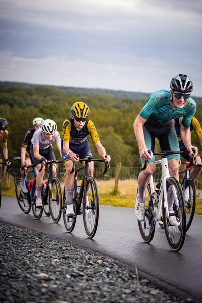 Junioren Mannen race cyclists wearing yellow helmets ride their bikes on the road.