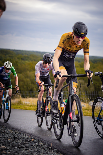 Three cyclists are wearing helmets and riding on a paved road.