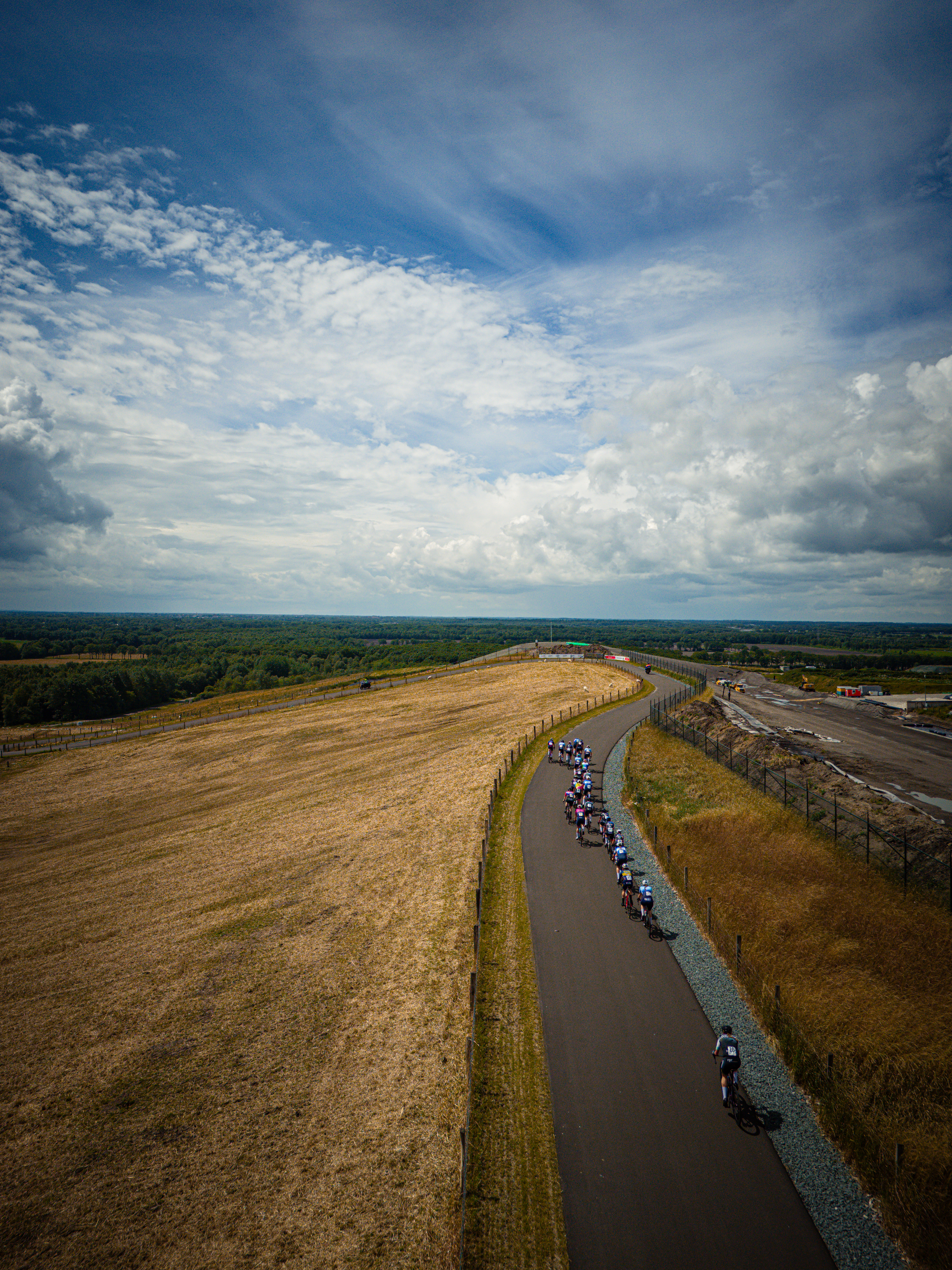 A group of riders are on a long path, the road is lined with gravel and grass.