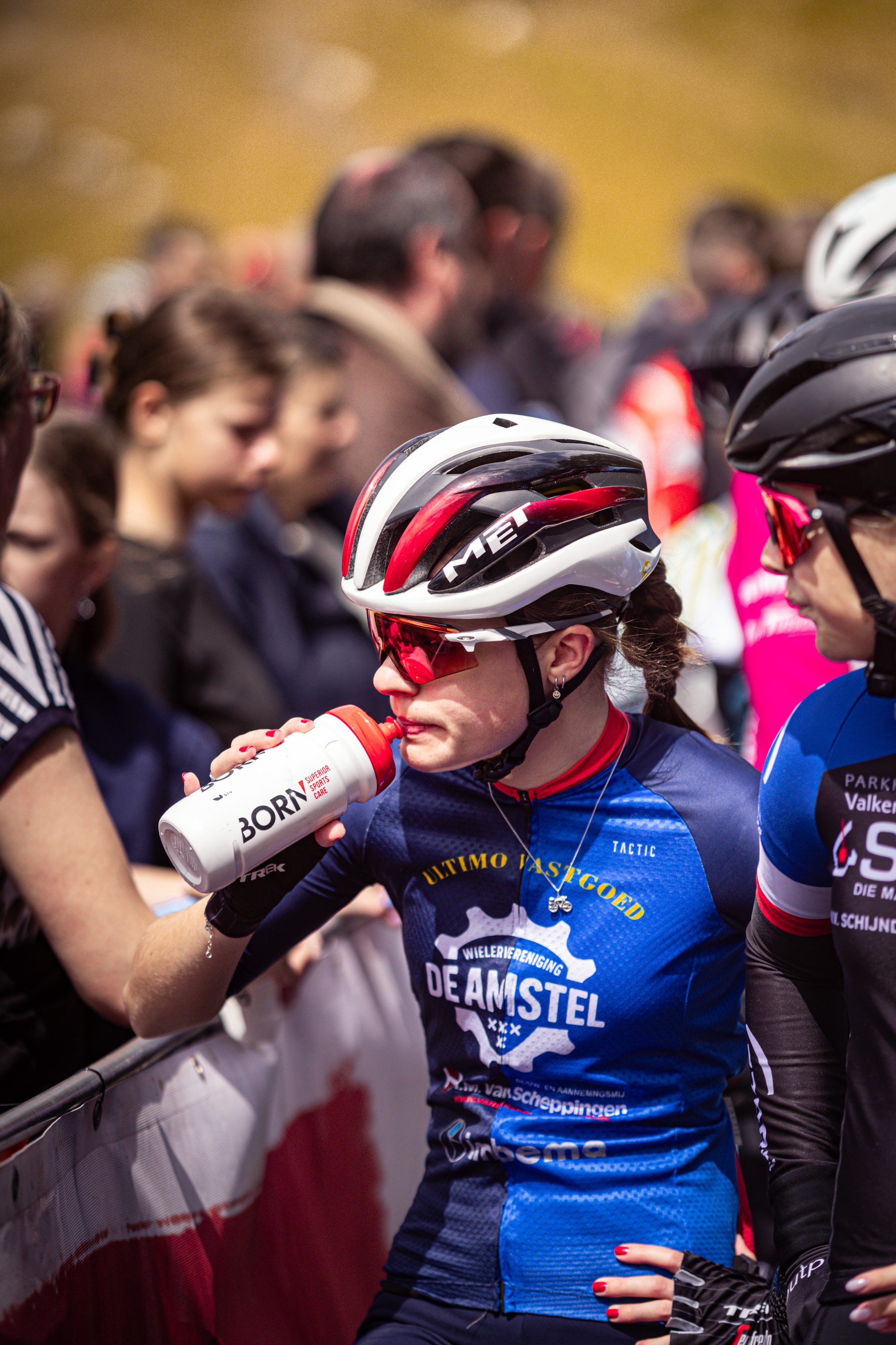 Two cyclists at a race, one is wearing a blue shirt with Deamstei written on it.