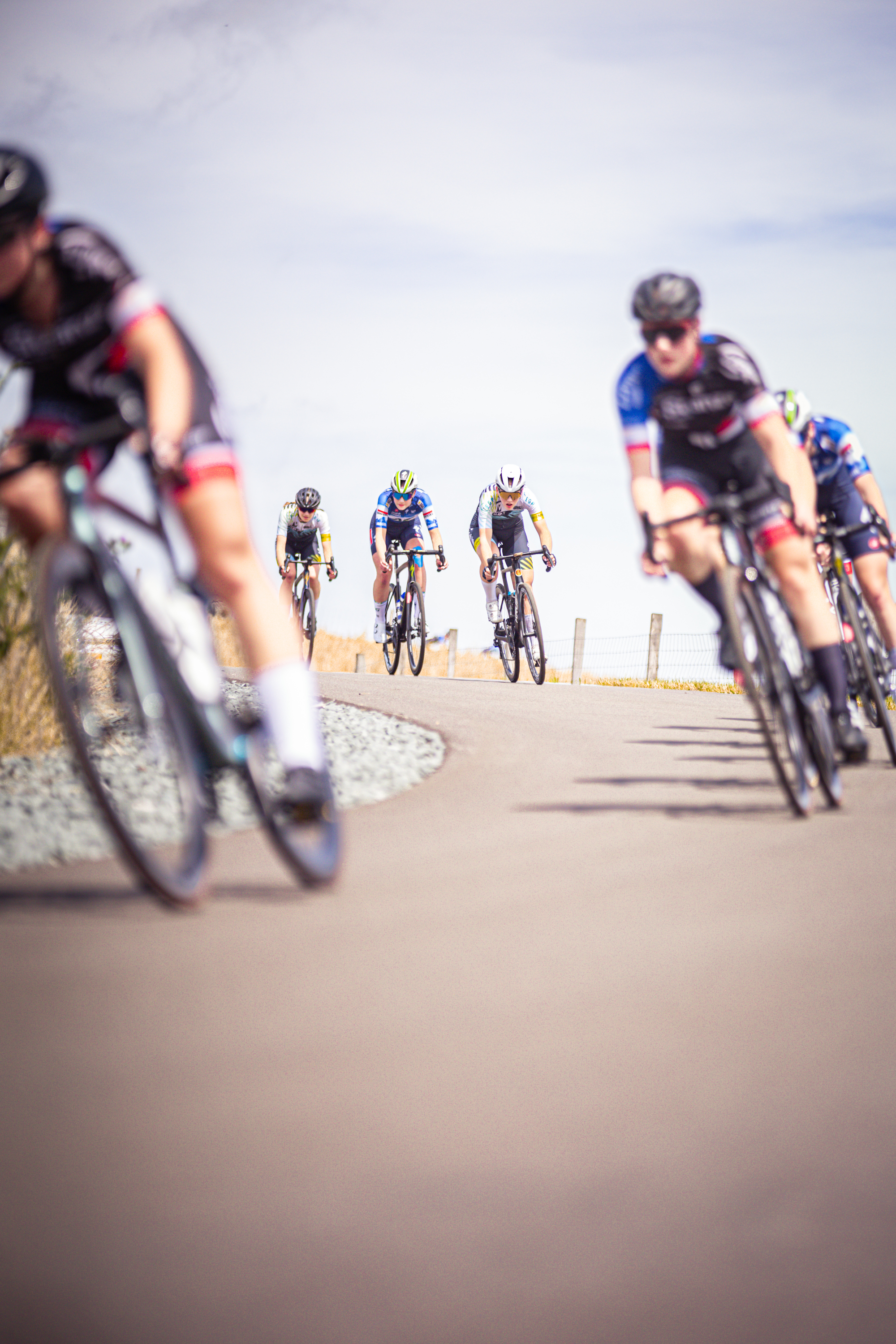 Several cyclists, including a woman in blue and black gear, are riding on a road during the 2024 Nederlands Kampioenschap.