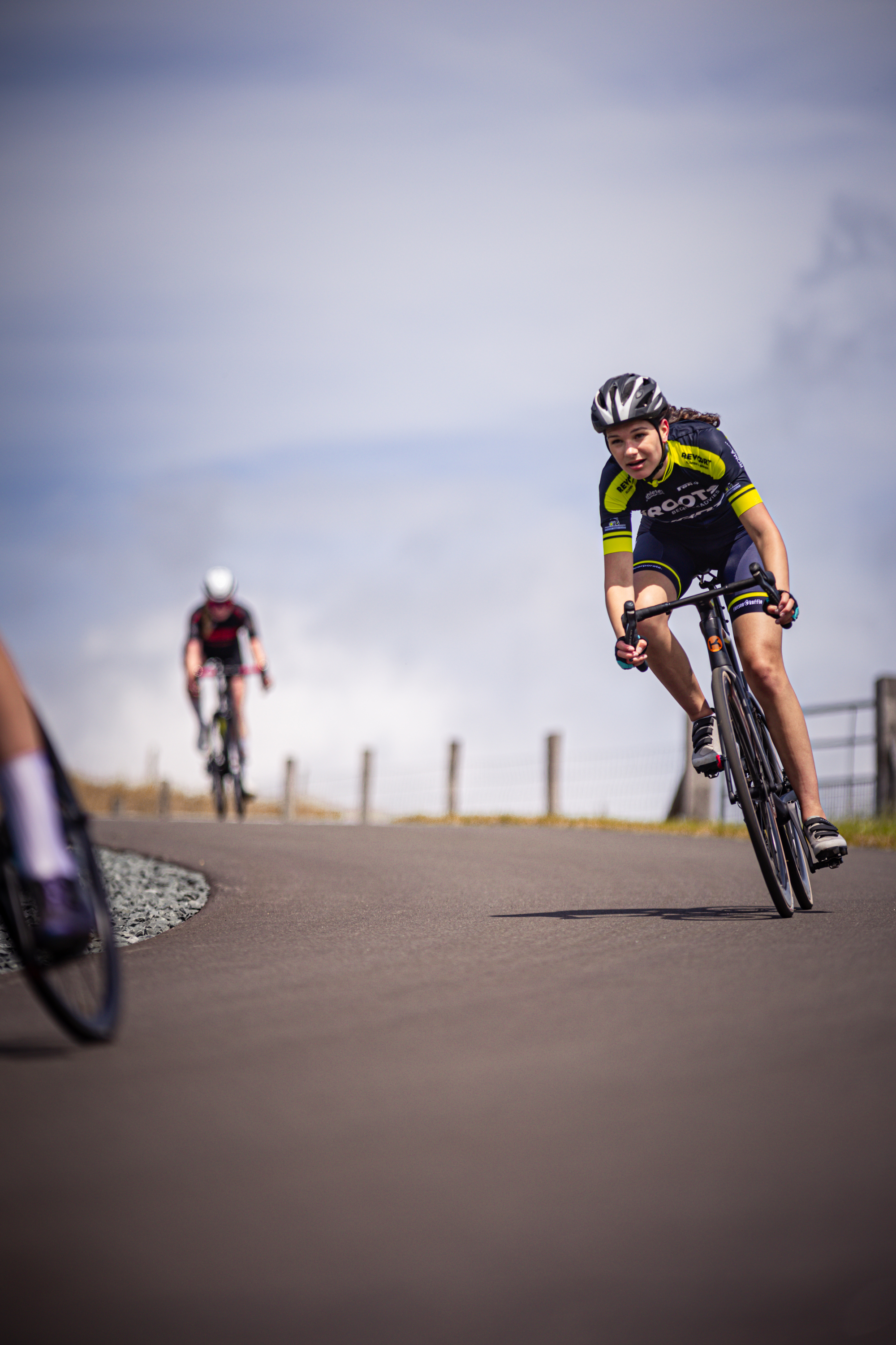 Two cyclists, including one in a yellow and black outfit, race on a road.