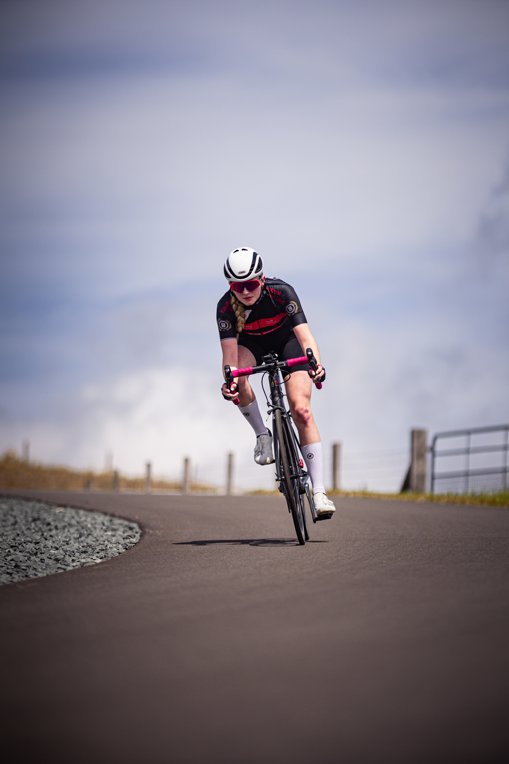 A woman riding a bicycle on the road, she is wearing an orange shirt and a white helmet.