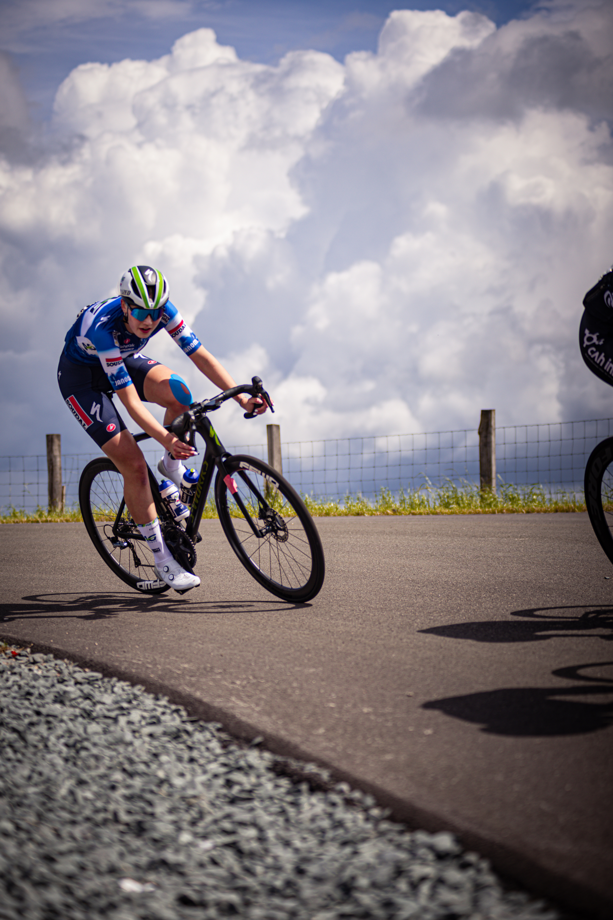 A bicycle racer wearing blue and black gears is riding a black bike with white tires.