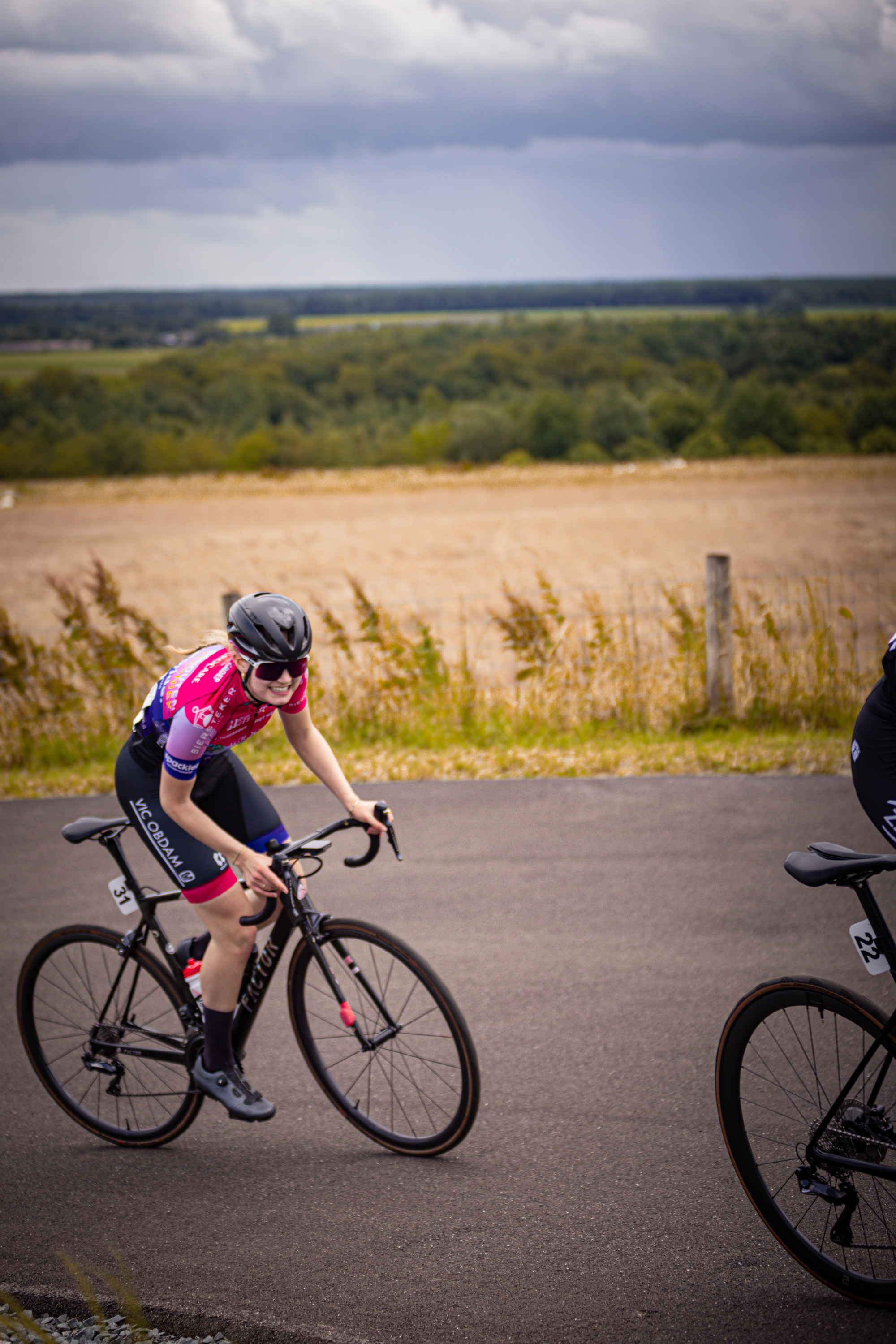 Two women riding bikes on a road with one wearing a pink jersey.