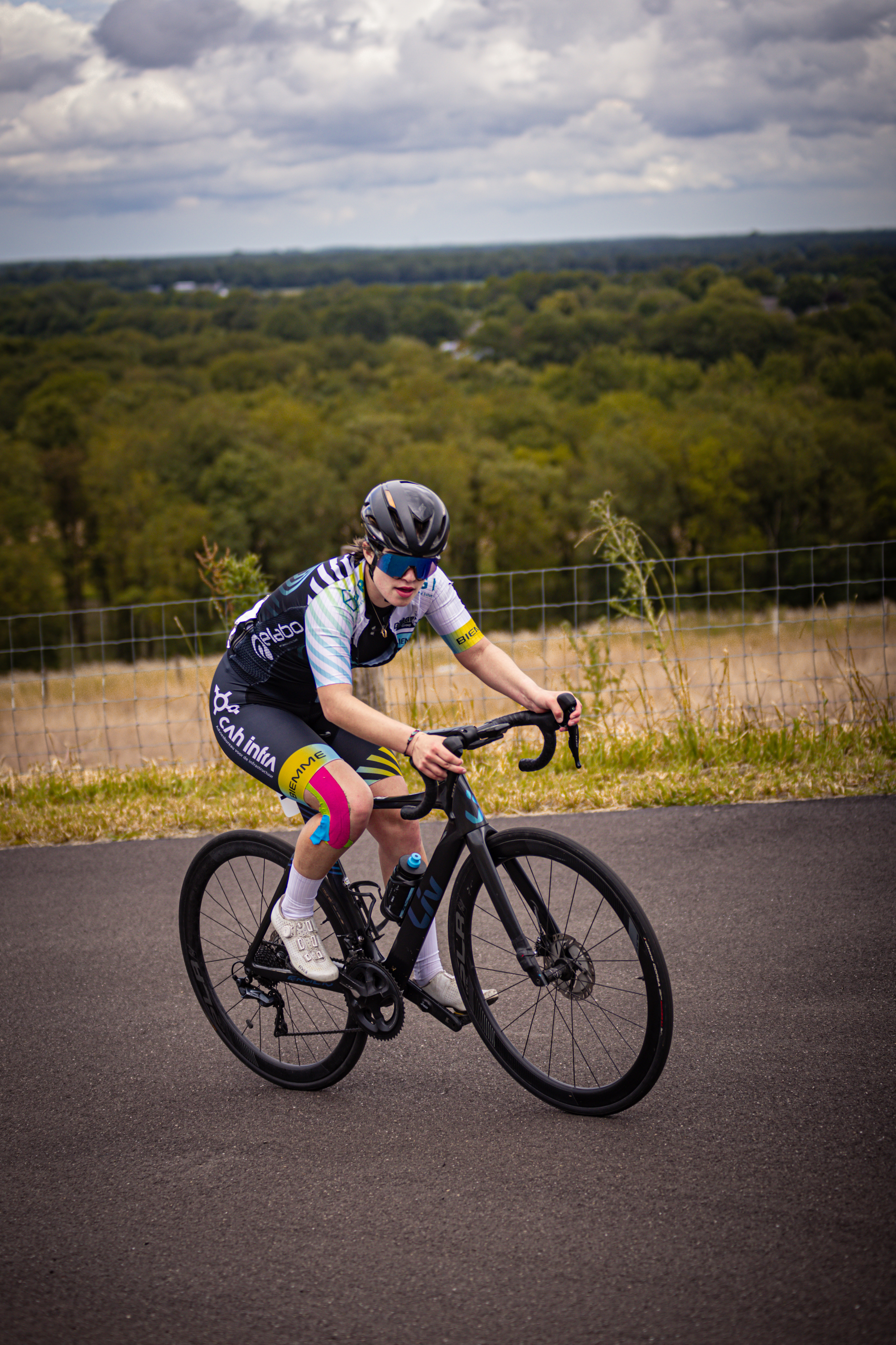 A young woman wearing a black helmet and a blue top with yellow lettering on it is riding a bike.