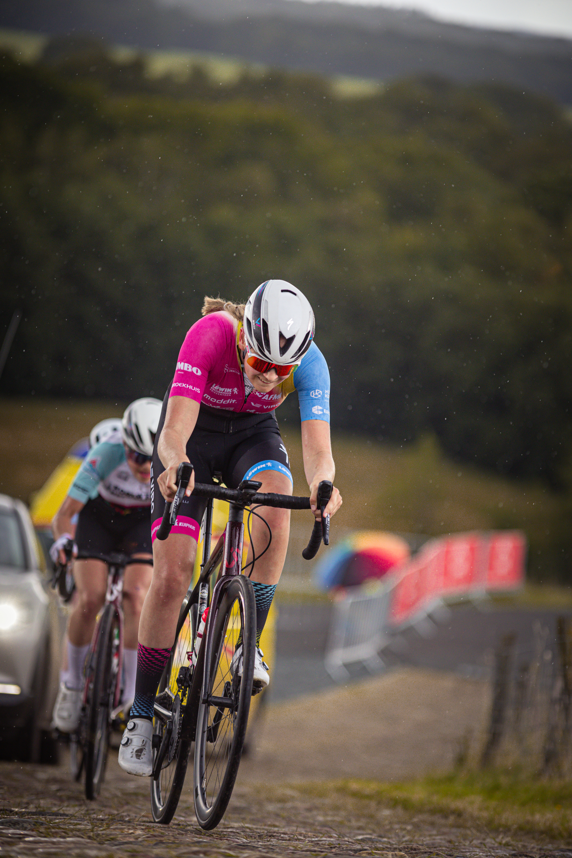 Two female cyclists riding on a trail. One is in the foreground and the other can be seen behind her.