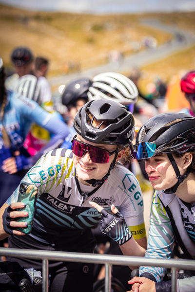 Two people wearing helmets pose for a photo at a race.