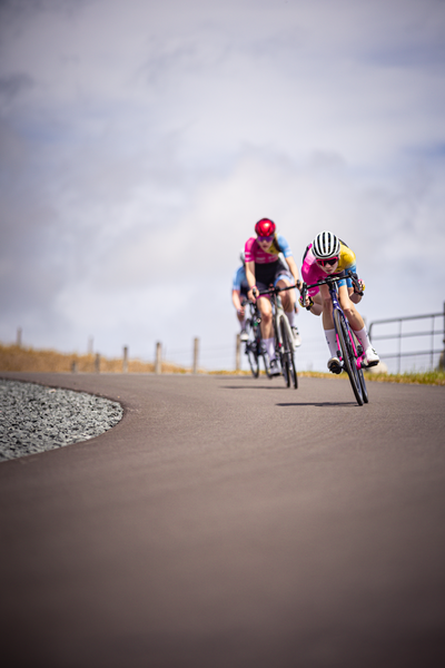 Three cyclists on a street, one with pink clothing and a yellow helmet.