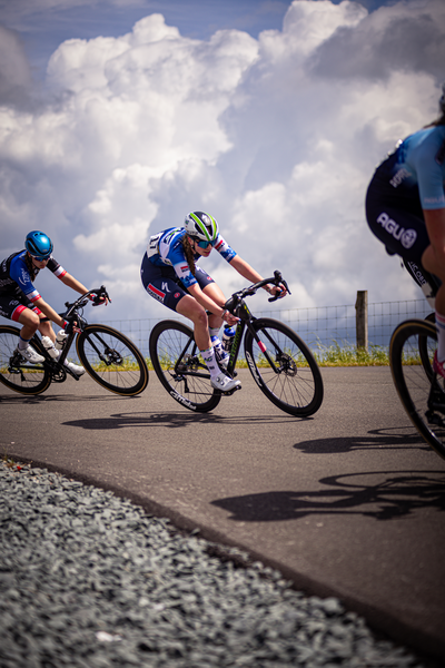 Three bicyclists are on a road for the Nederlands Kampioenschap Wielrennen.