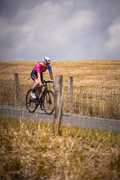 A female cyclist with a pink jersey is riding her bike on the road.