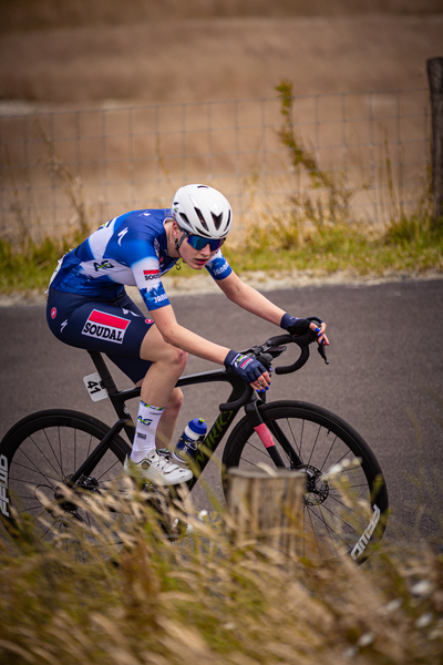 A young boy wearing a blue and white track suit rides his bicycle on the road.