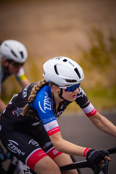 A young woman is in motion, wearing a white helmet and blue and red cycling clothes.