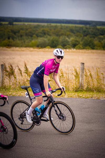 A person wearing a pink jersey is riding a bike on the road, they are wearing white gloves and a white helmet.