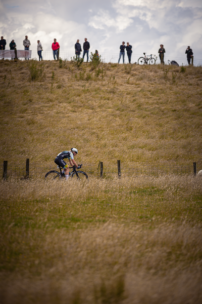 A man is riding his bike in a field as people look on from the top of a hill.