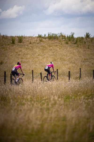 Two cyclists on a grassy field with one wearing a pink and white jersey.