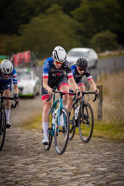 Bike racers on a cobblestone road. They are all wearing blue and black with red accents, and helmets.