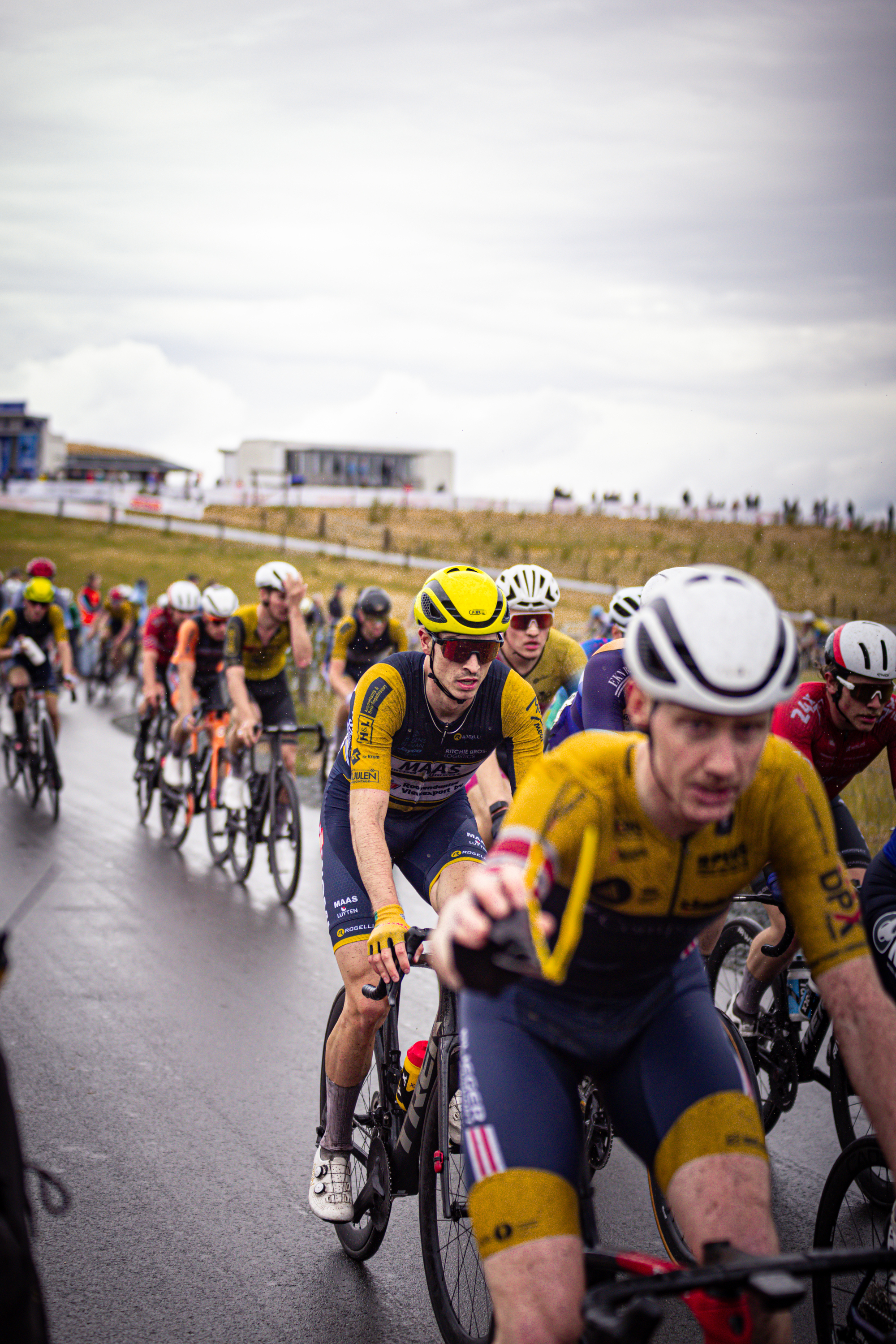 A group of cyclists wear matching yellow and blue uniforms as they ride through a grassy area on the track.