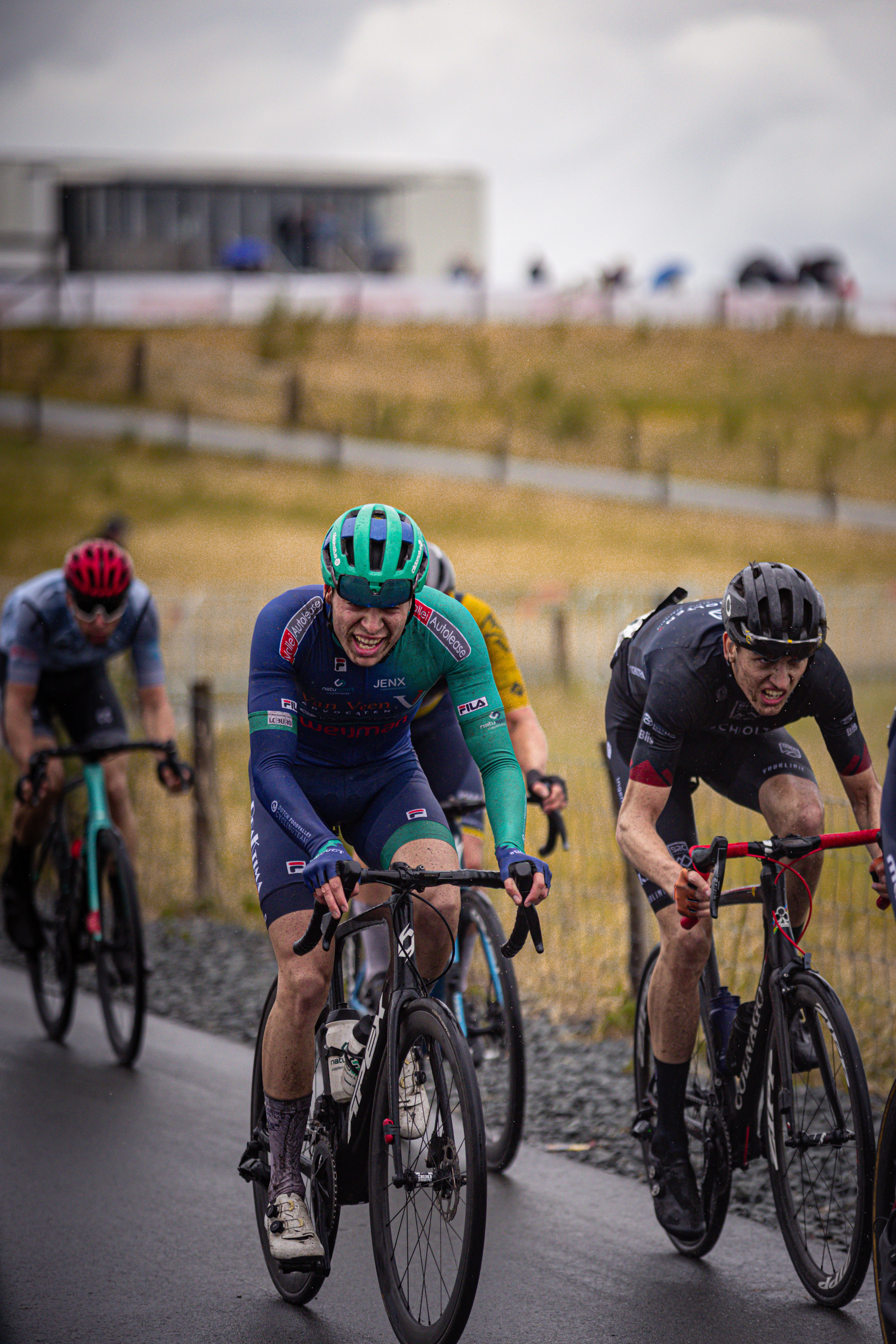 A group of cyclists are riding on the road. They are all wearing helmets and racing jerseys with numbers on them.