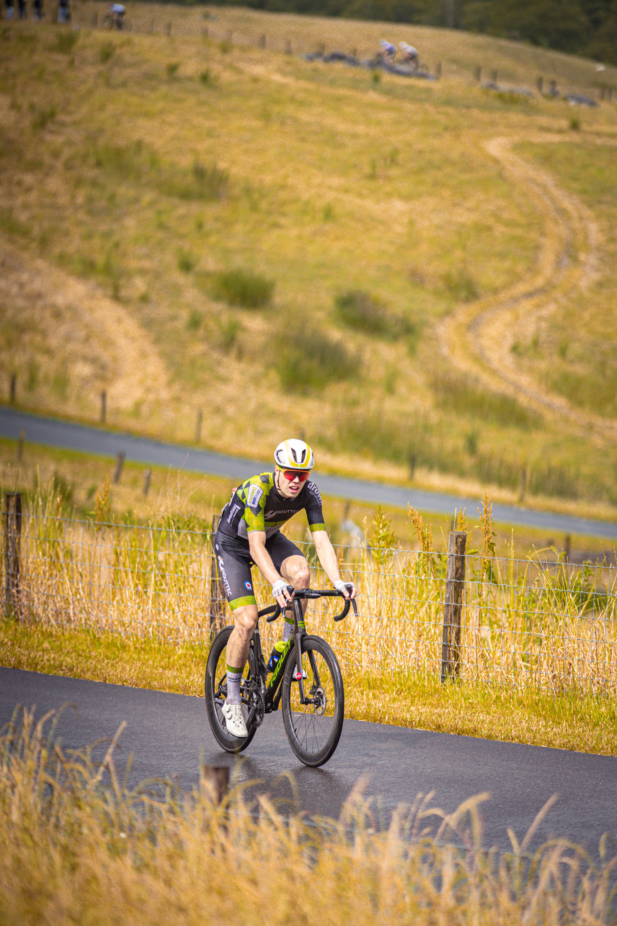 A rider in a black and yellow shirt rides his bike down a hill.