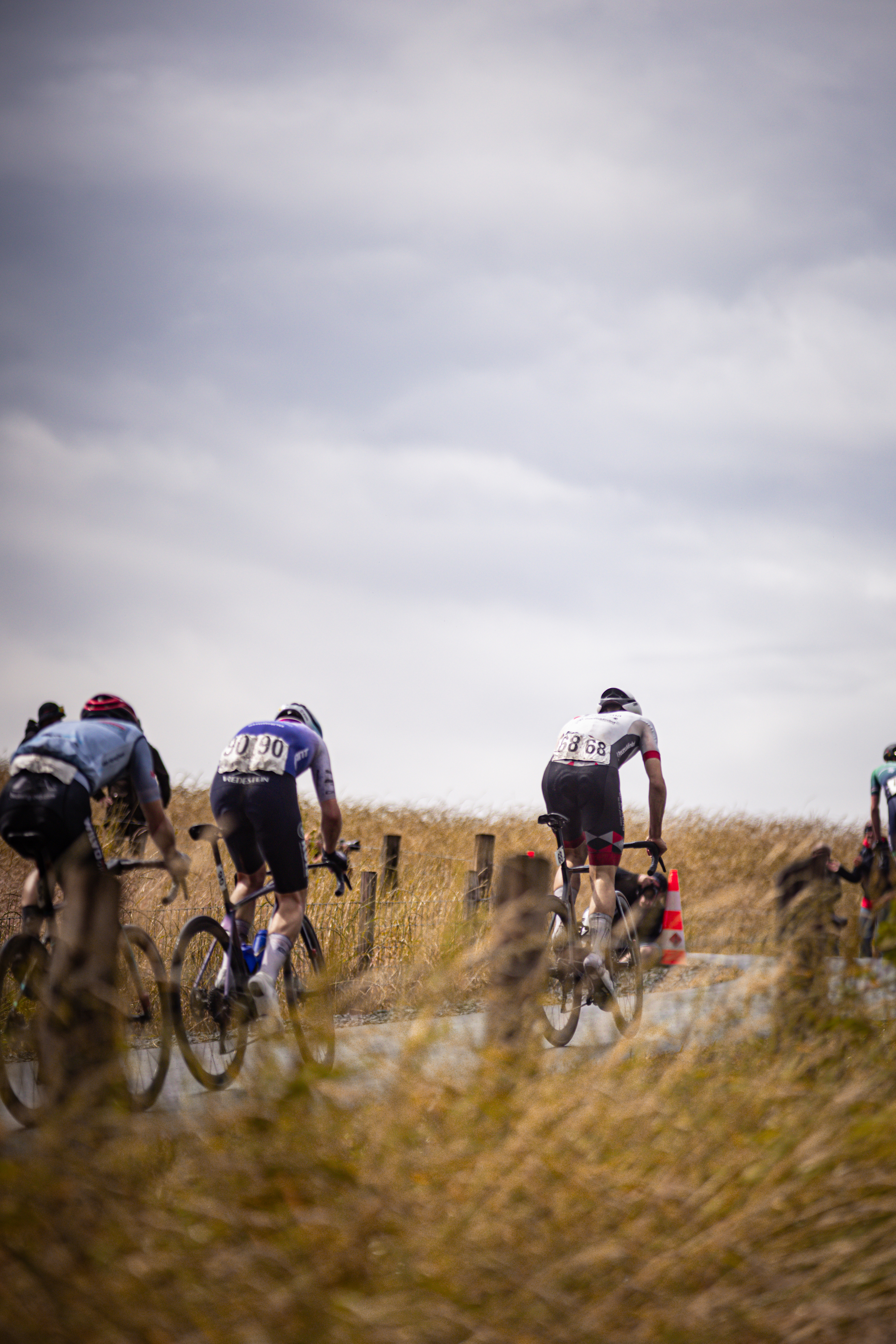 Three cyclists riding in a field and one wearing the number 2 on his back.