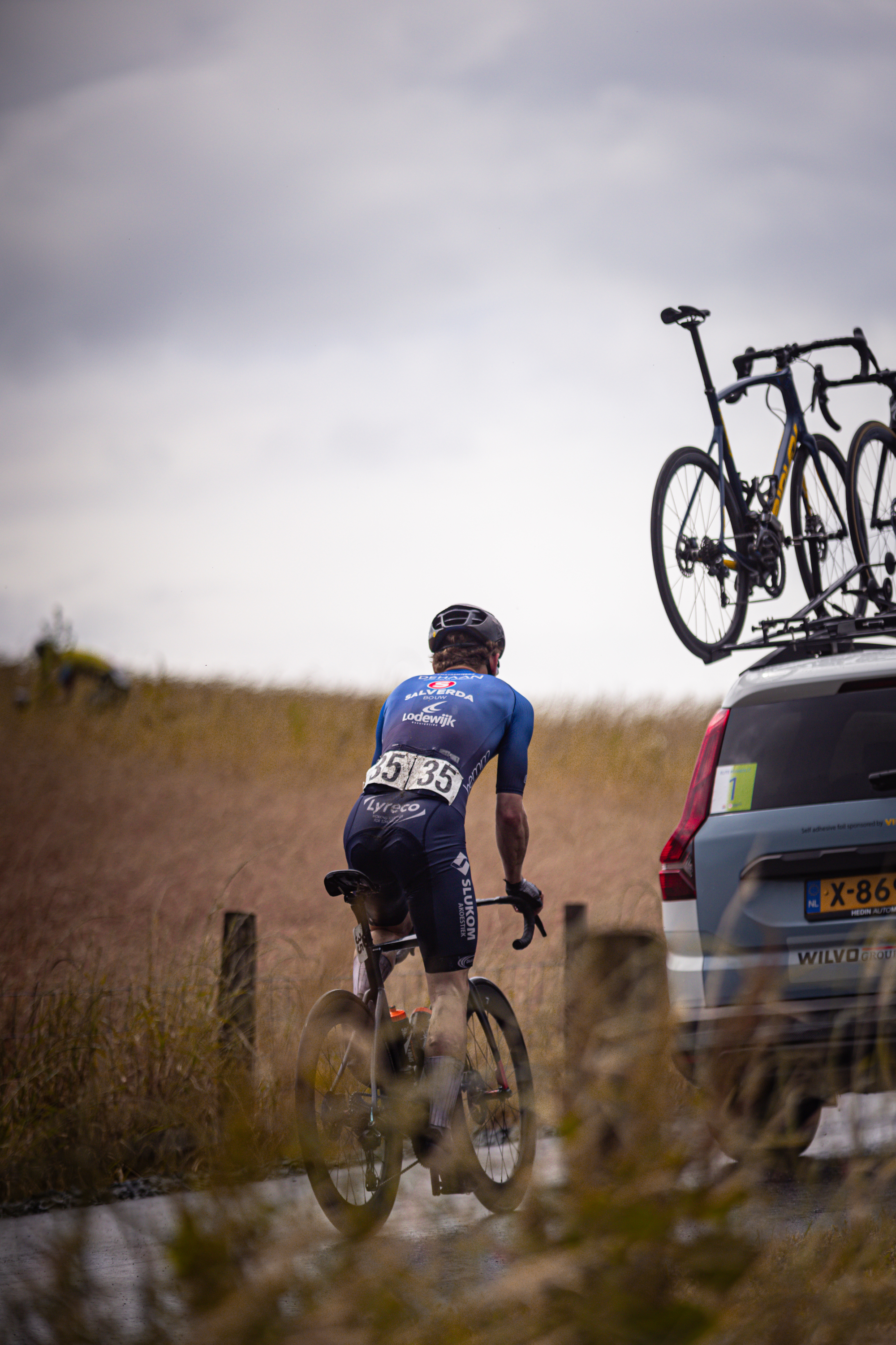 A man in a blue jersey is wearing a helmet as he looks at the bicycle mounted on his car.