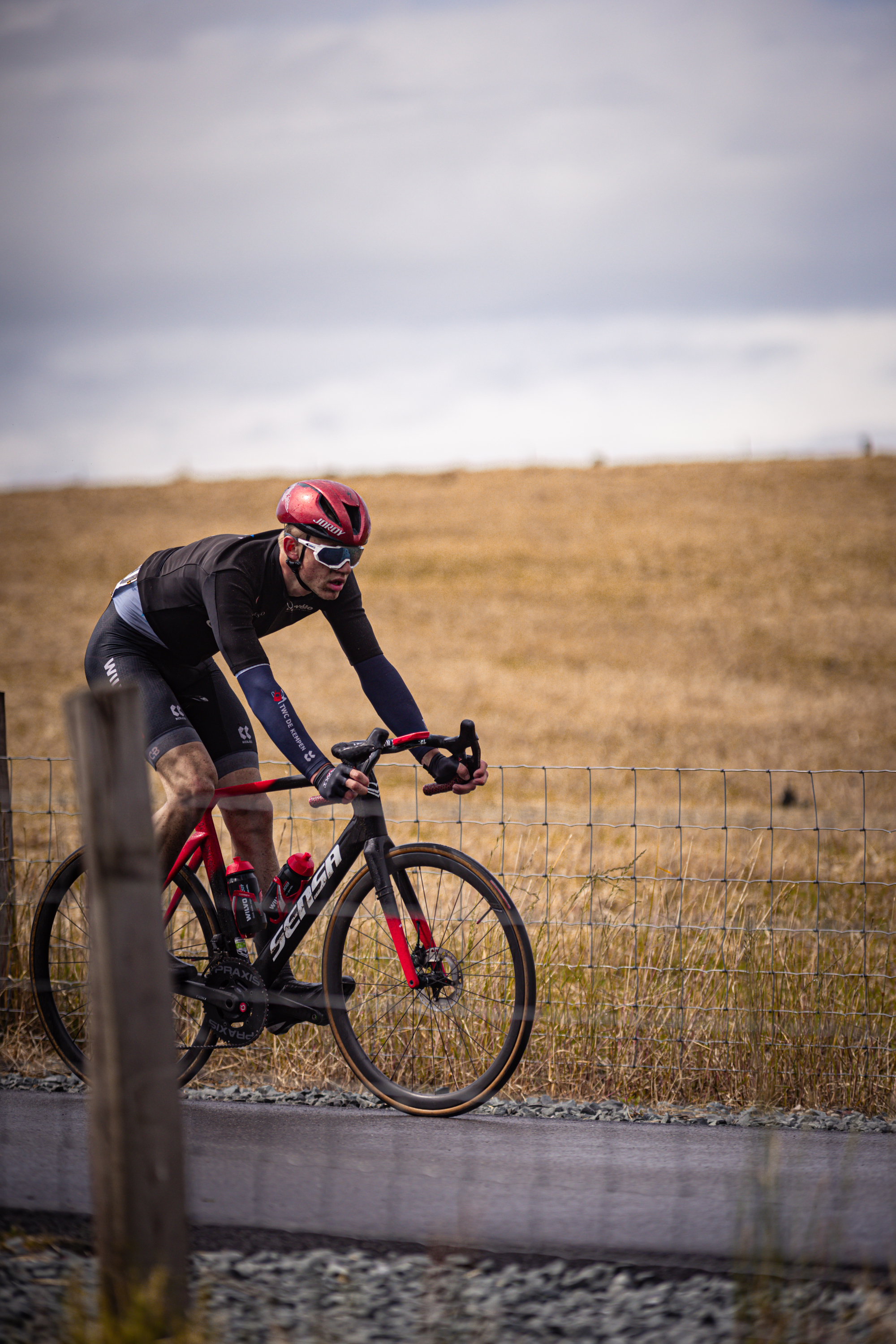 A cyclist wearing a black jersey is riding his red bike on a track.