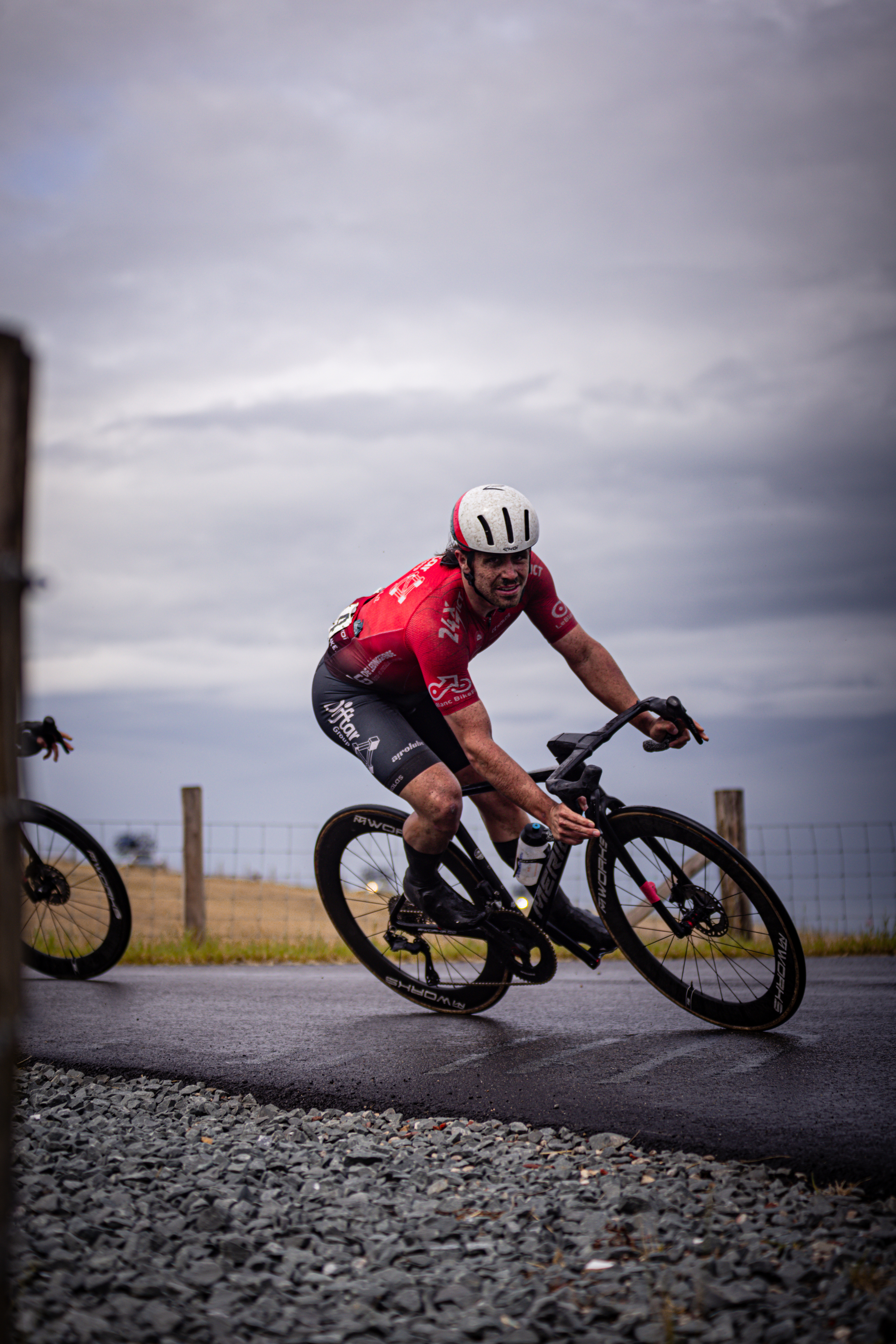 A man in a red and black racing jersey is riding a bike on the road. He has a helmet on for safety.