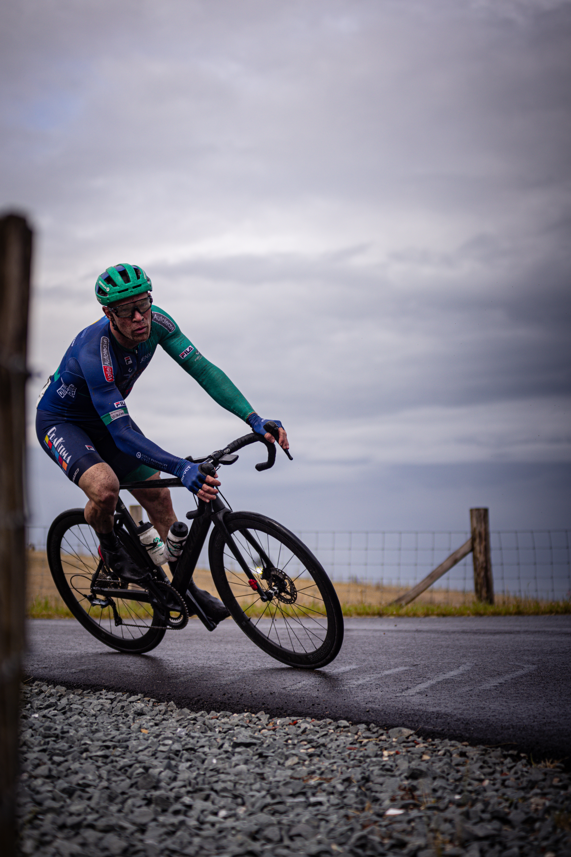 A man on a bicycle wearing a blue, green and black uniform with the word "Wielrennen" on it.