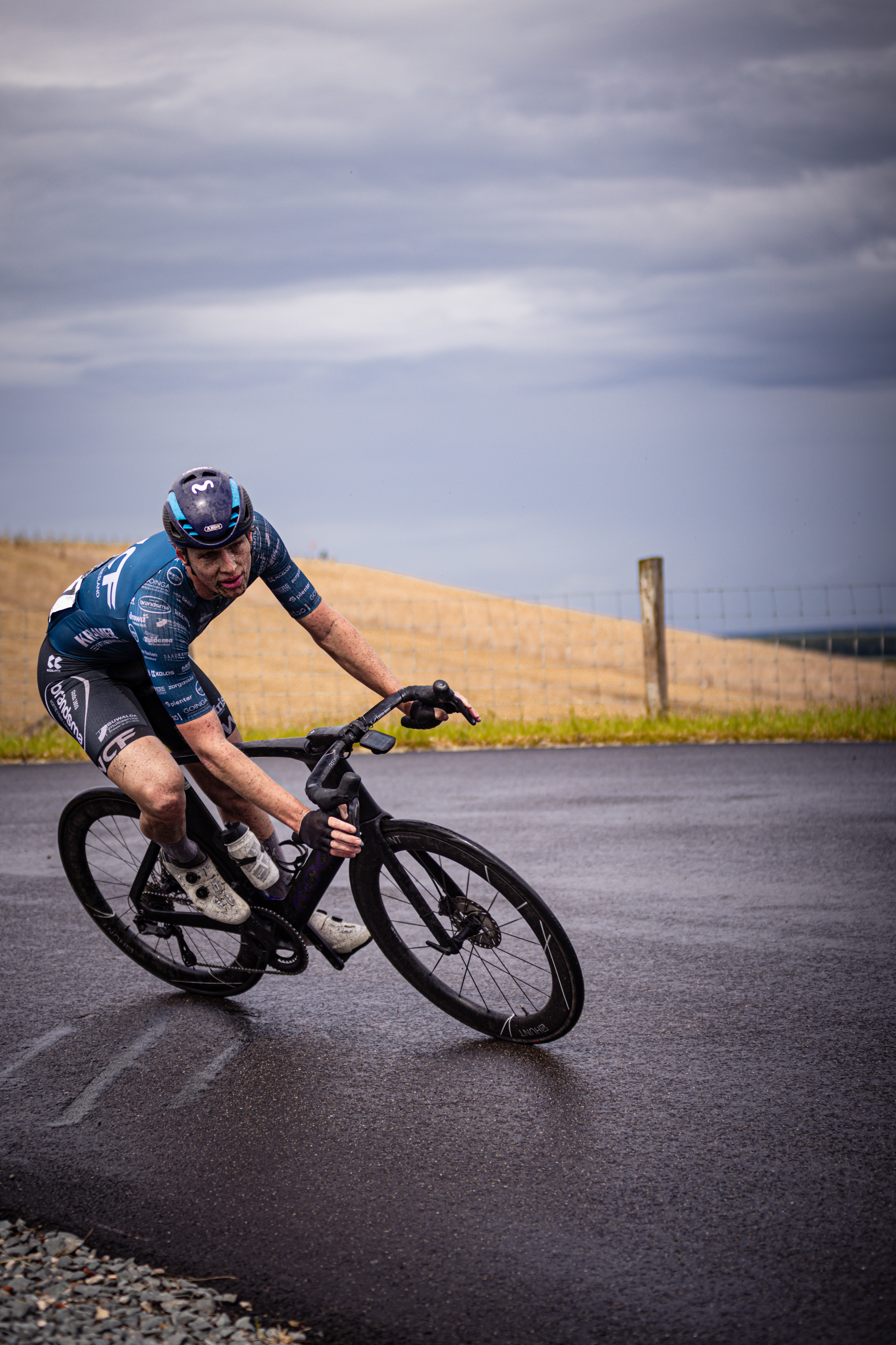 A man is riding a bike down the street, wearing blue and black.