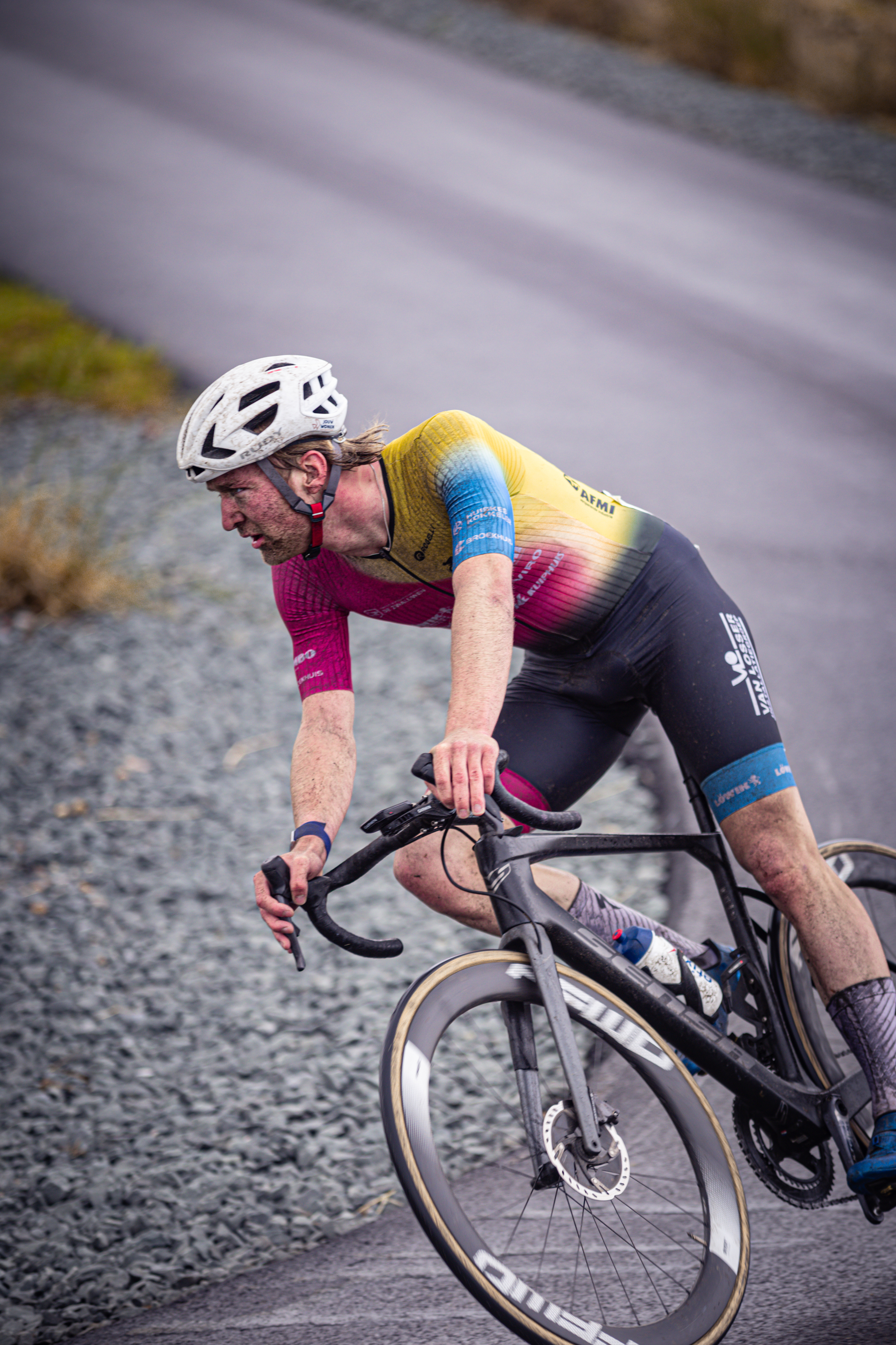 A man is riding a bike on a street while wearing his team uniform.