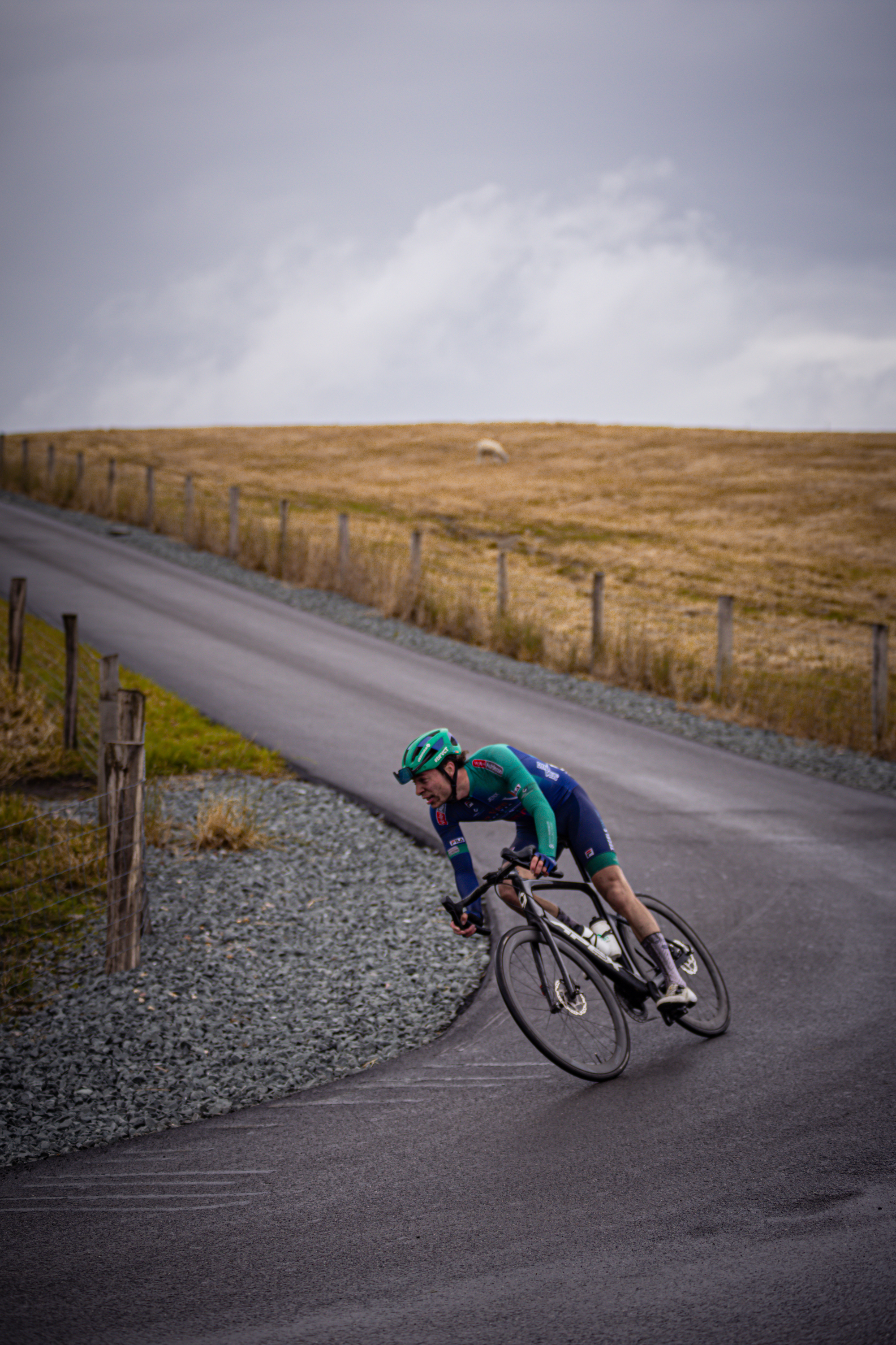 A man wearing a blue and green jersey rides his bike on a road.