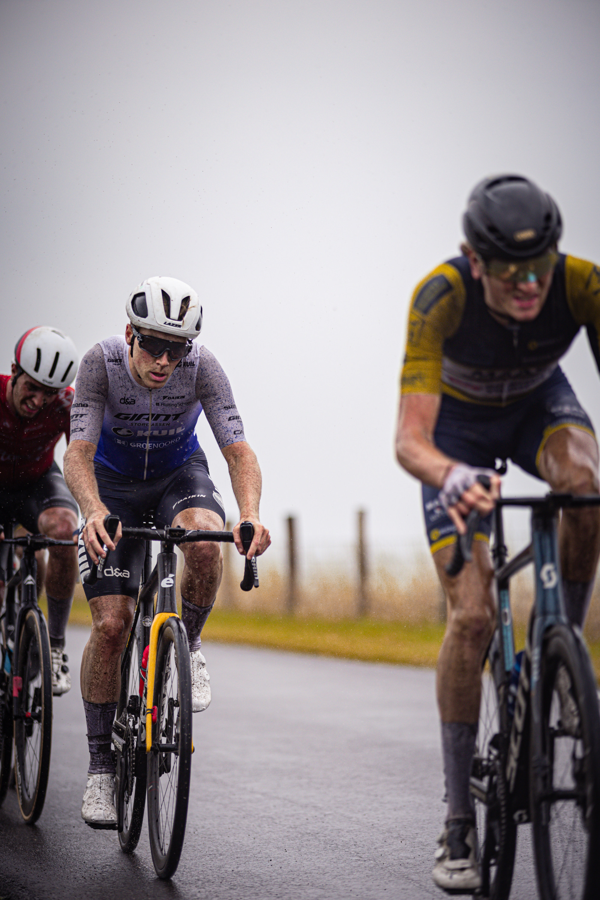 A man wearing a yellow and black jersey is riding his bike down the road ahead of others.