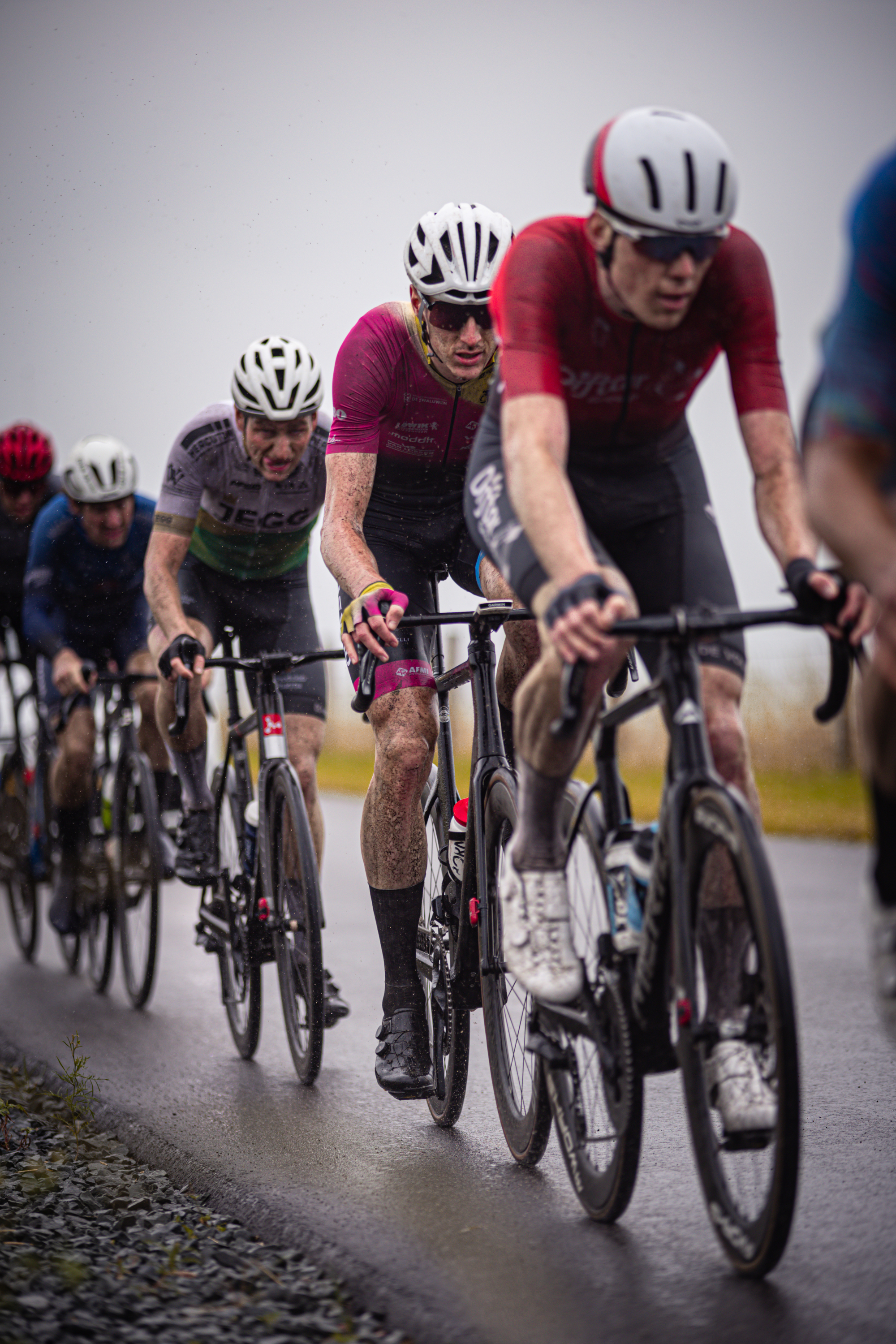 Several men are riding bicycles down a wet road during the 2024 Nederlands Kampioenschap for Mannen Elite ZC.