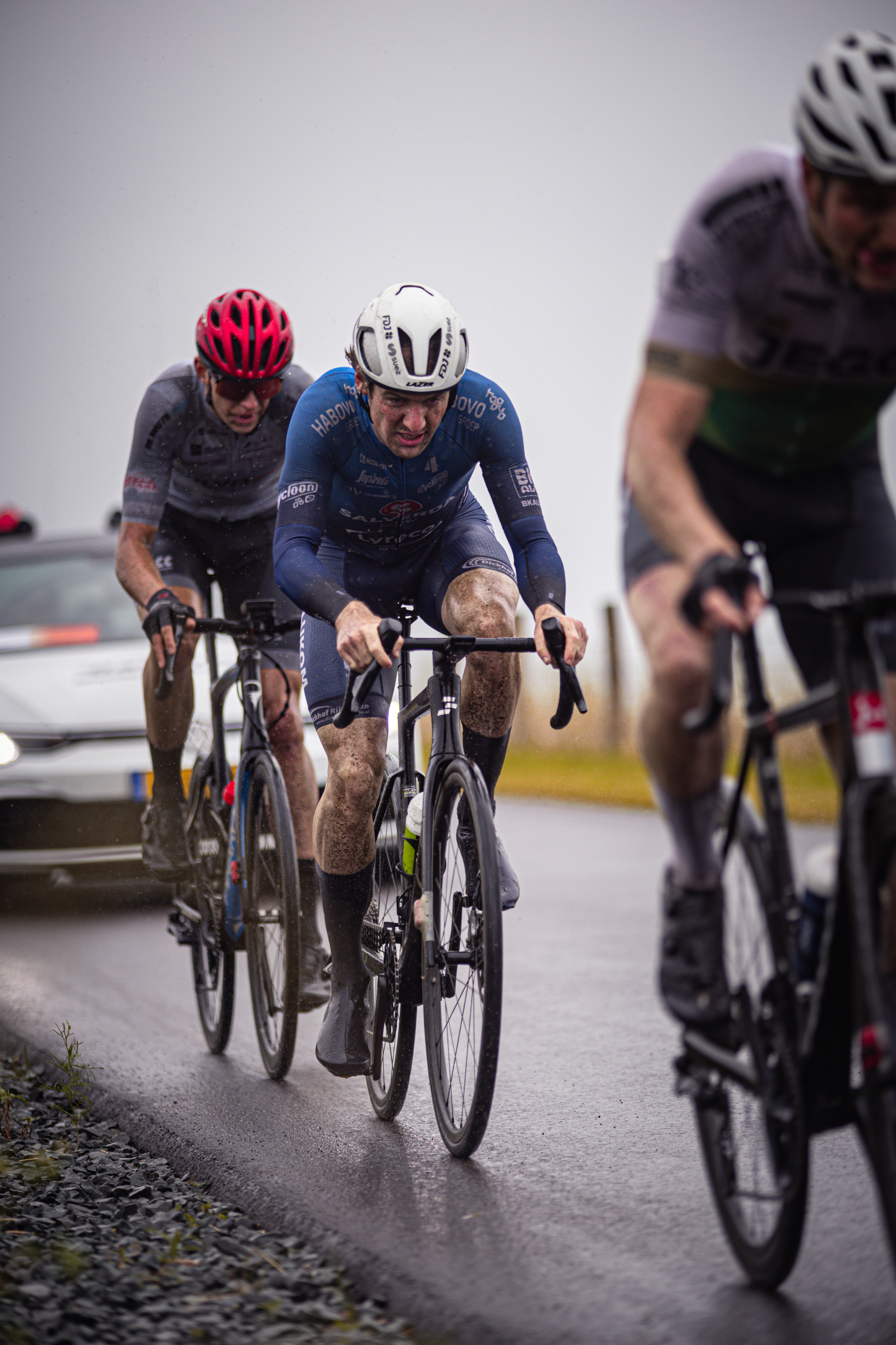 Three cyclists wearing helmets are riding down a wet road.