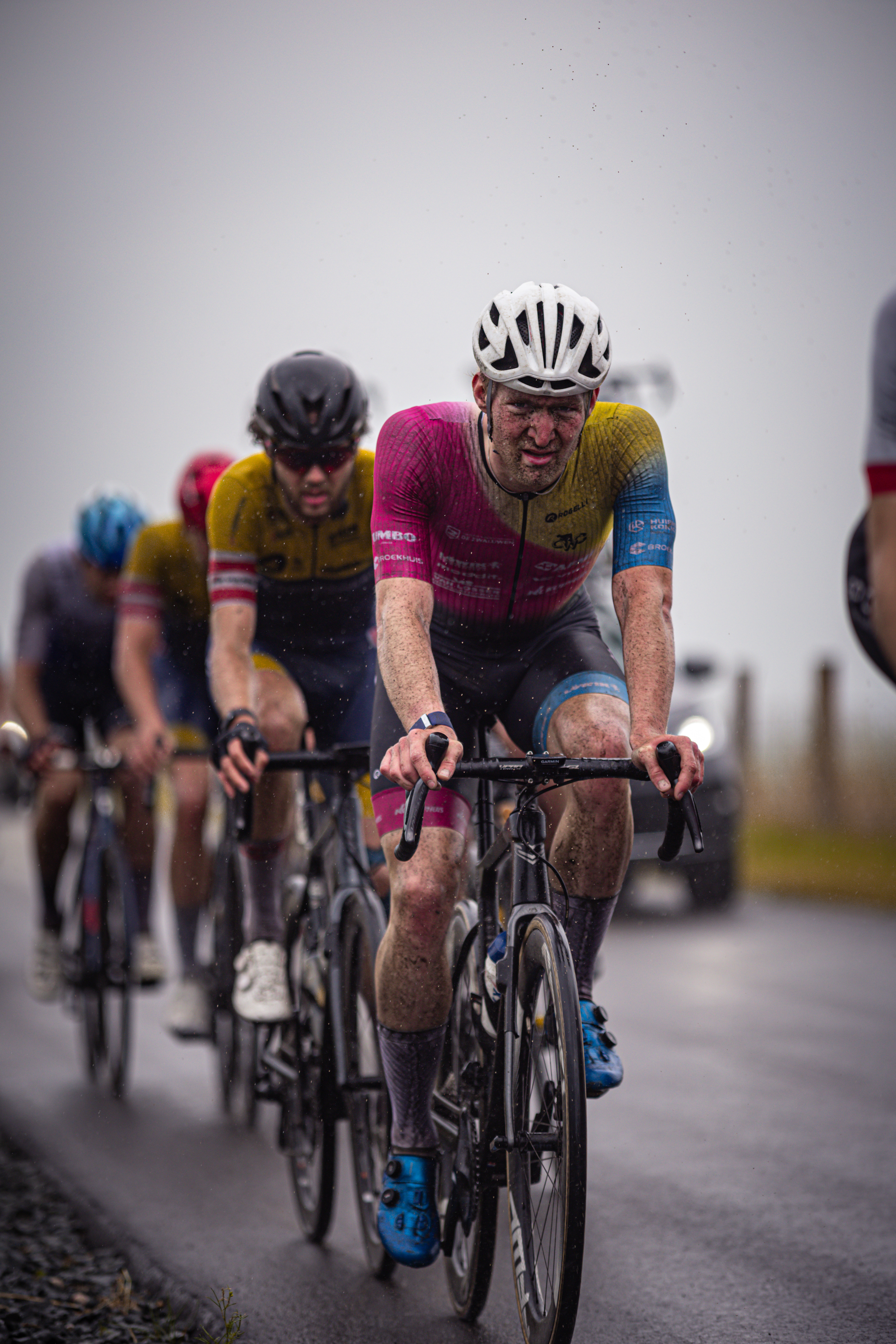 Three cyclists racing down a road with one in pink and yellow jersey.